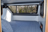 Relax in this cozy RV rental bed with serene forest views from the large window. Features a fan and handy bedside pocket storage.