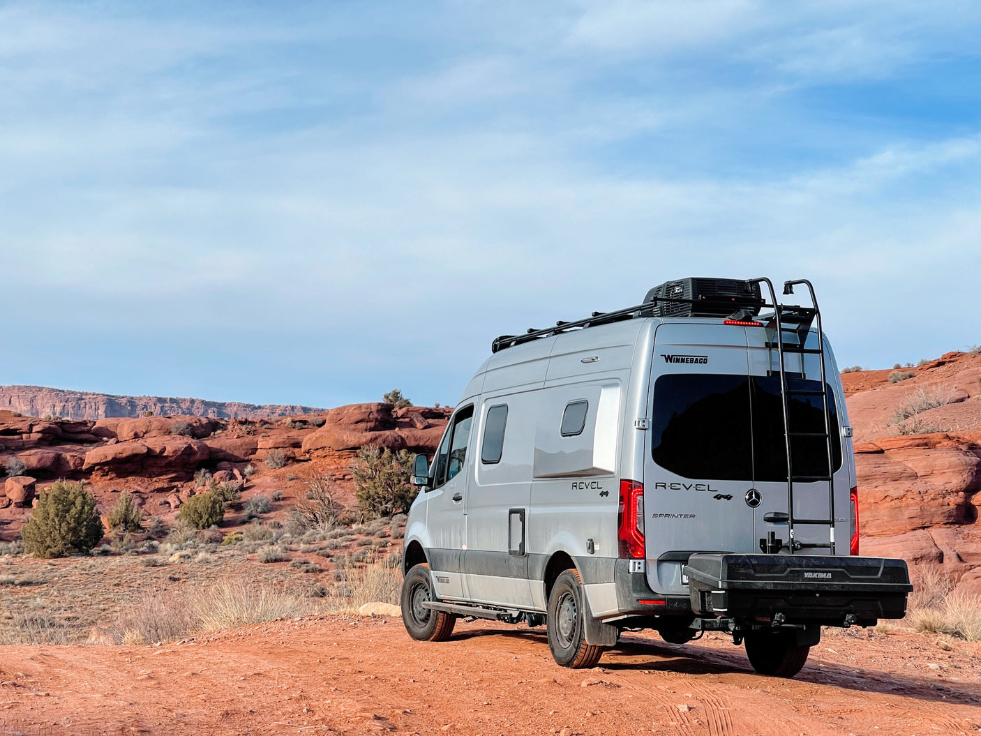 Winnebago Revel 4x4 RV rental parked on a red desert road, surrounded by stunning red rock formations.