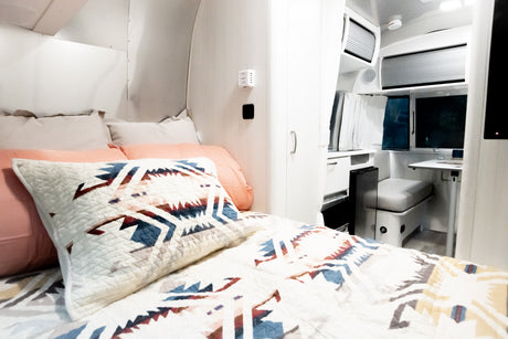 Modern RV rental interior showcasing a cozy bedroom with patterned bedding and a compact dining area.