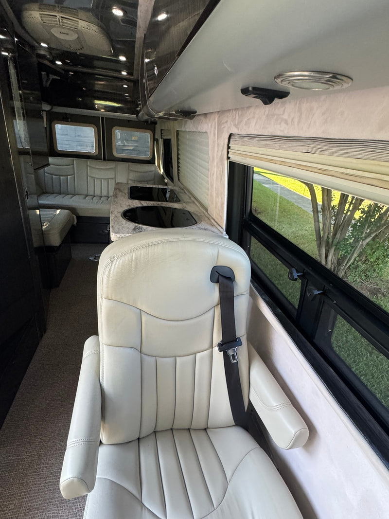 Luxury RV rental interior showing a cream captain's chair, kitchen prep area, and cozy rear lounge seating. — photo 10