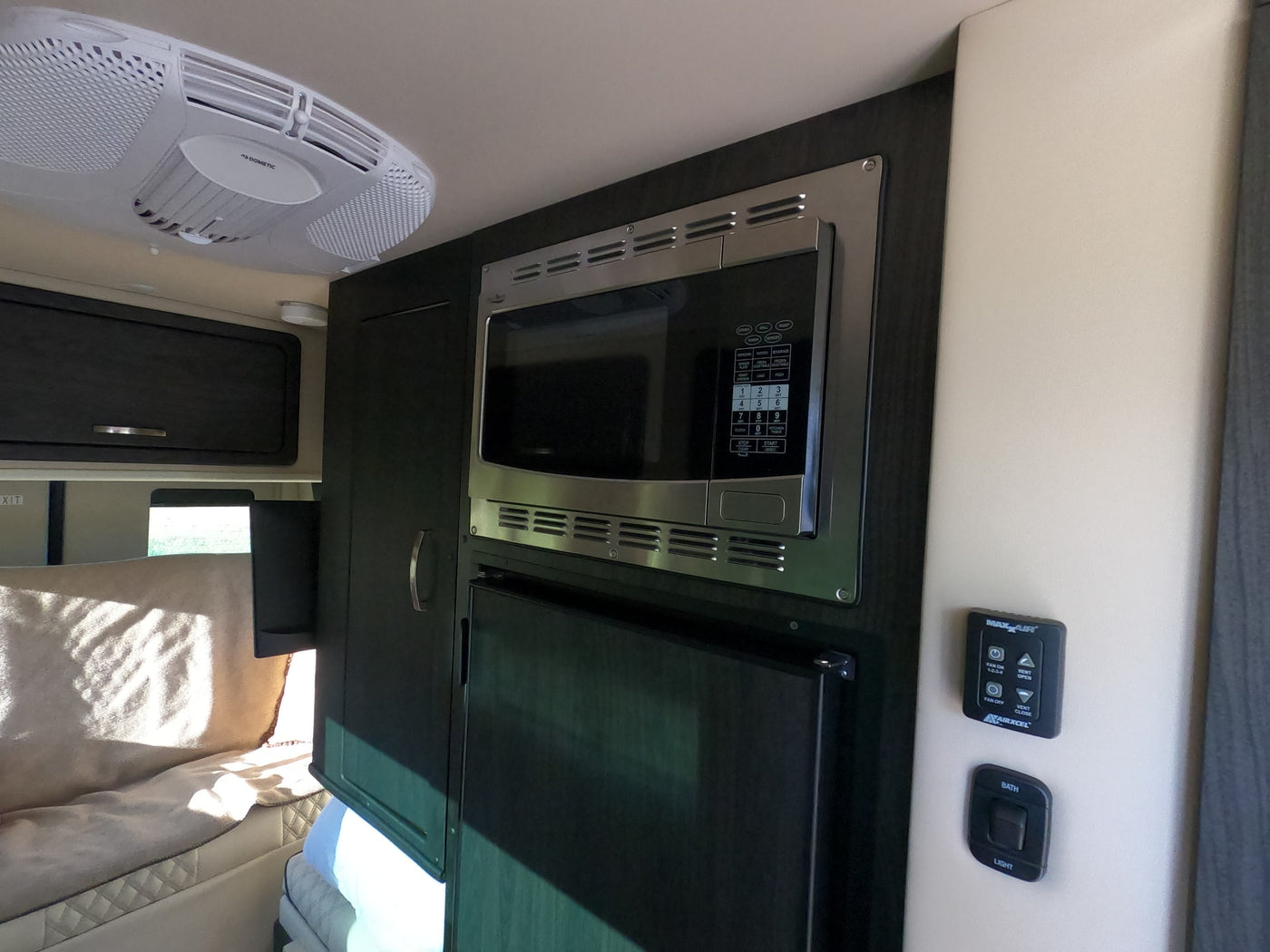 An RV rental interior showing a Dometic AC, microwave, fridge, and MaxxAir controls for comfort on the road. — photo 9