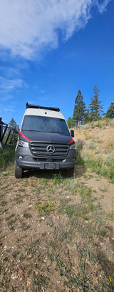 Grey Mercedes Sprinter adventure van, possibly an RV rental from Titan Vans, parked on a dirt path under a blue sky.