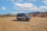 Adventure awaits! This rugged rv rental, parked on a dirt lot, is perfect for exploring mountains & deserts under a blue sky.