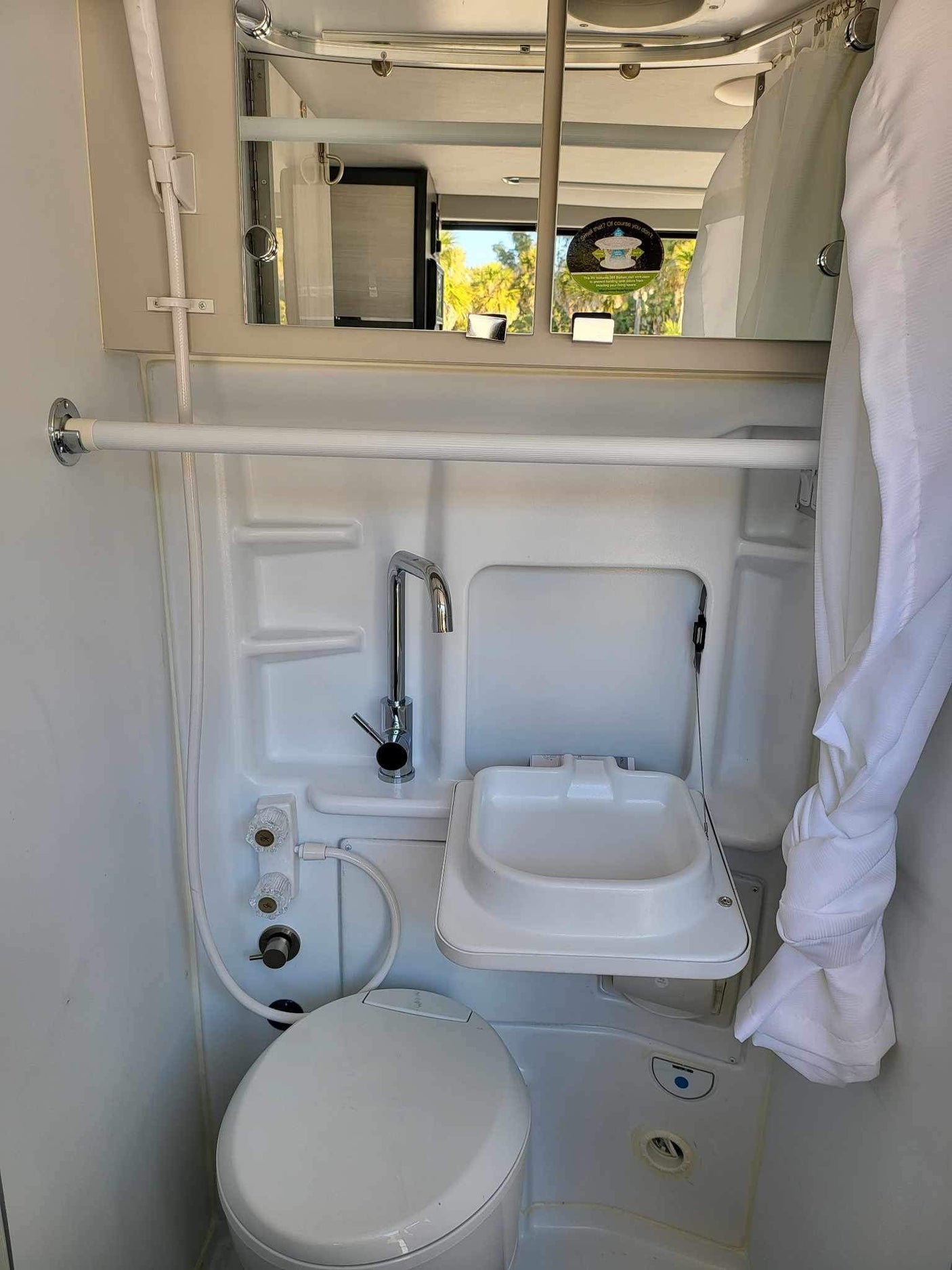 Compact wet bath in an RV rental, featuring a toilet, sink, and shower. Ideal for travel convenience.