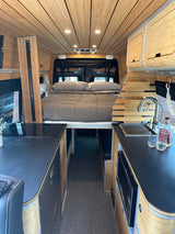 Spacious RV rental interior featuring a bamboo-paneled ceiling, comfy bed, modern induction stovetop, and sink.