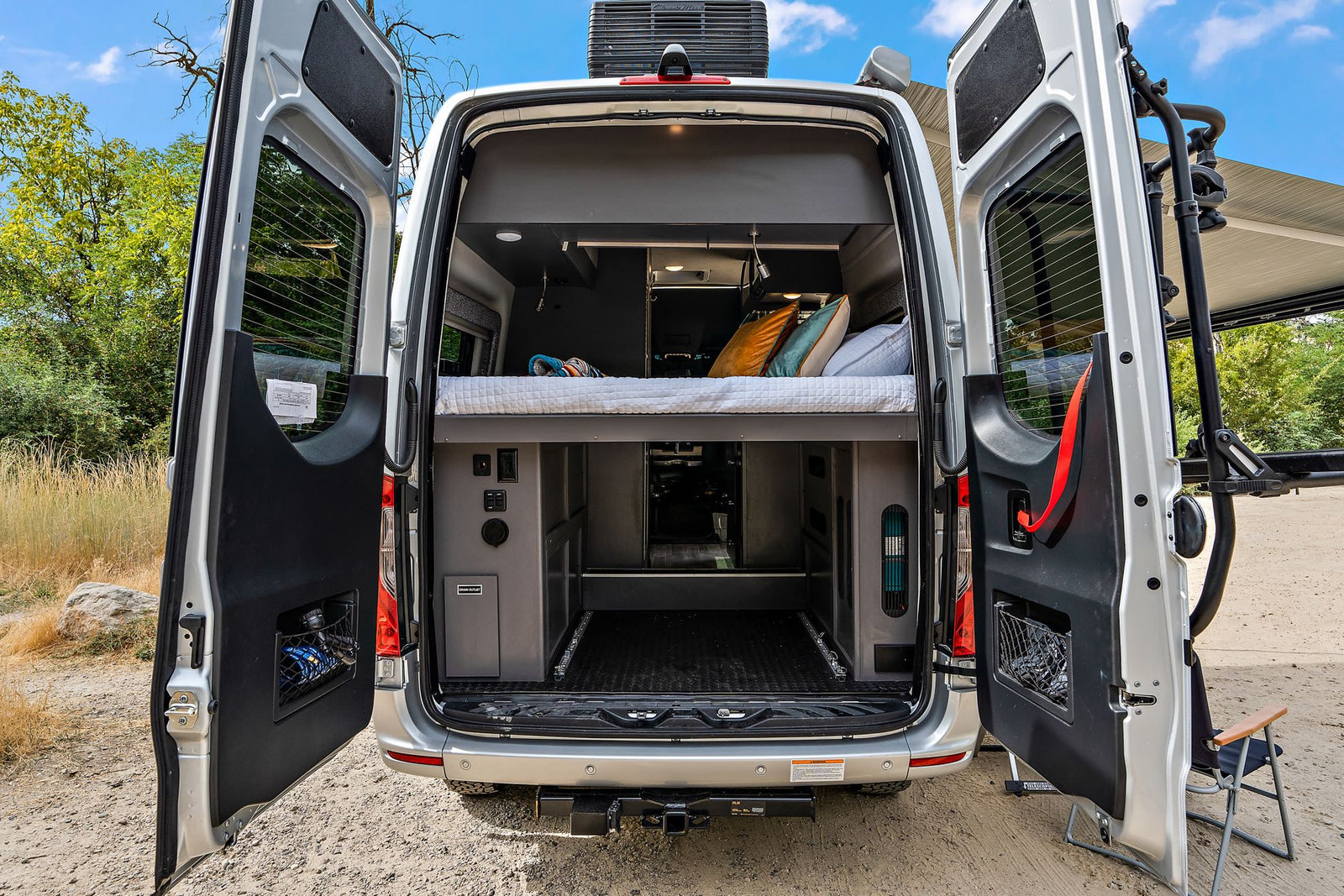 Open rear of a silver RV rental, showcasing its comfortable bed, versatile storage, and accessible cargo area.