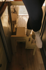 Stepping into an RV rental using a wooden step stool. A person in black leggings and white socks enters a cozy interior.