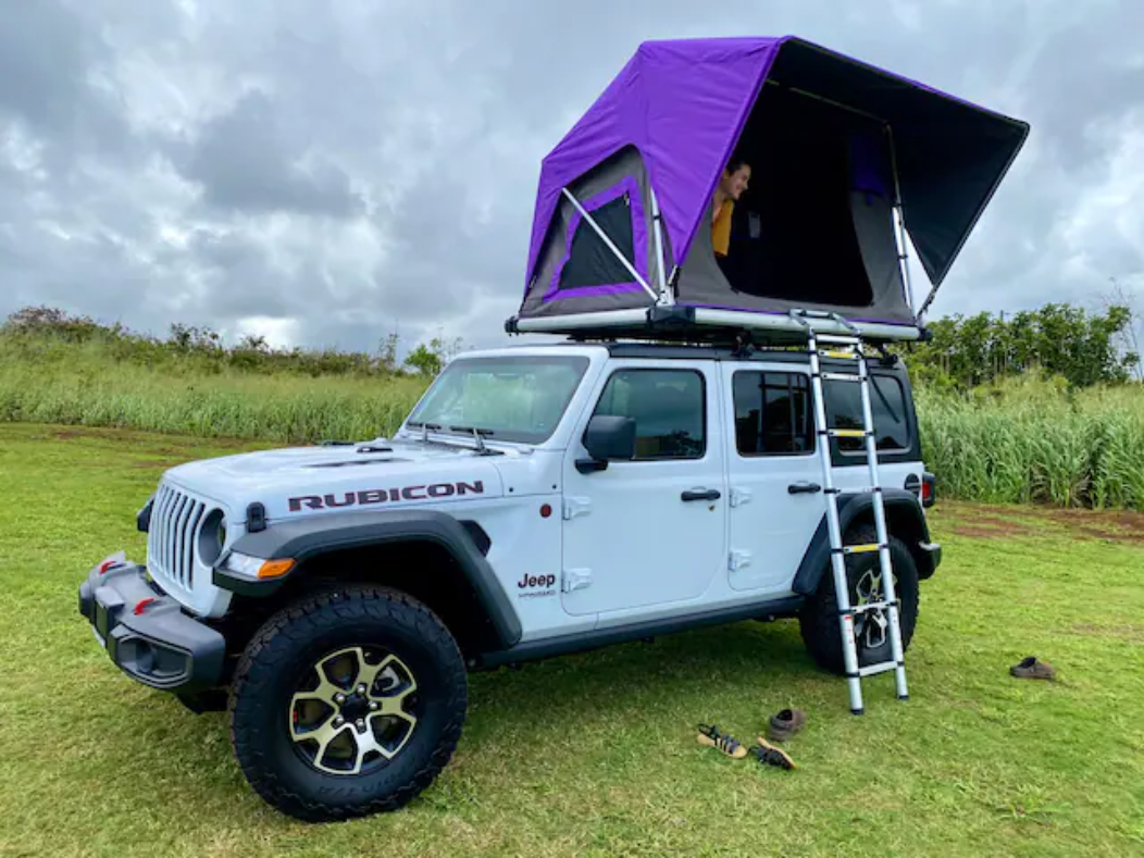 White Jeep Rubicon with purple rooftop tent and ladder, person inside. An ideal rv rental for overland camping adventures!