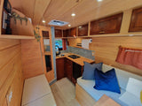 Explore this warm RV rental interior: light wood, functional kitchen with stove & sink, cozy seating, and ample storage.