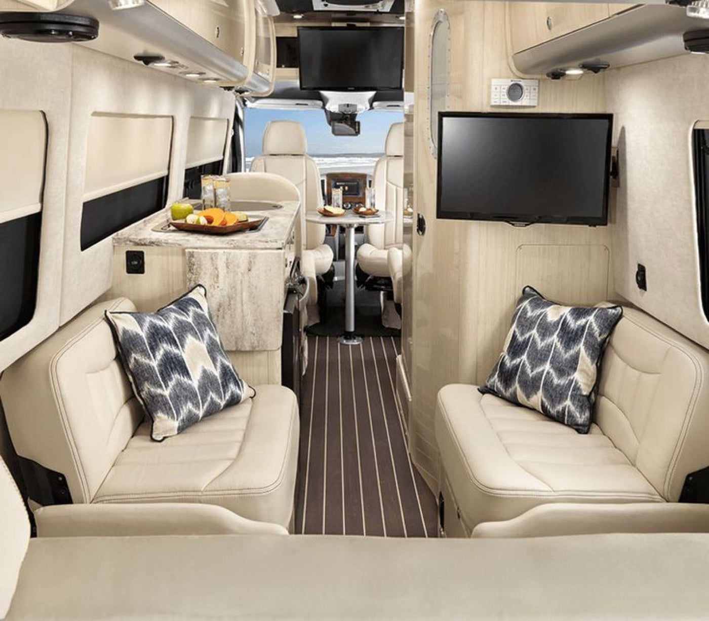 This luxury RV rental interior features comfy seating, a kitchen, TV, and a dining area, with a beach view through the front. — photo 6