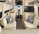 This luxury RV rental interior features comfy seating, a kitchen, TV, and a dining area, with a beach view through the front.