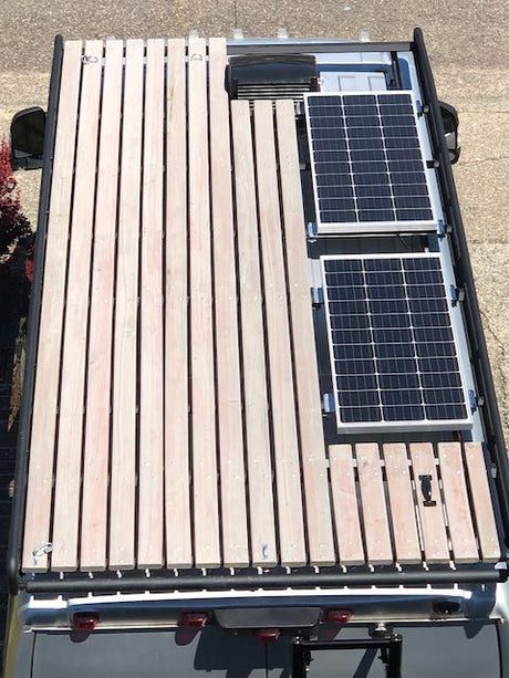 Rooftop view of an rv rental van featuring two solar panels and an expansive slatted wood deck. Ideal for extra cargo or outdoor living.