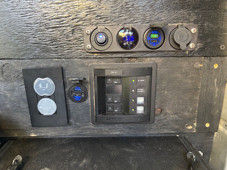 RV rental: Electrical control panel with AC/DC power outlets, USB charging, voltmeter (13.6V), and circuit breakers.