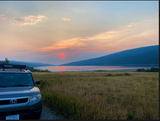 A grey Honda Element with a roof rack overlooks a stunning lake sunset in Montana, a great spot for an rv rental trip.