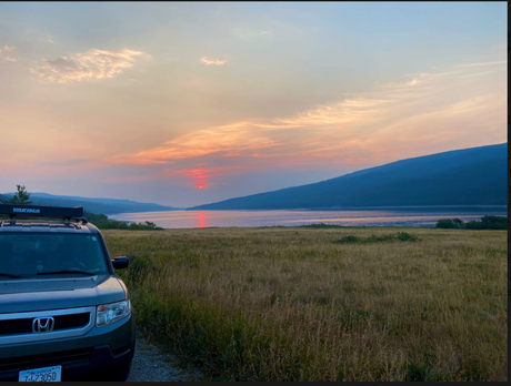 A grey Honda Element with a roof rack overlooks a stunning lake sunset in Montana, a great spot for an rv rental trip.