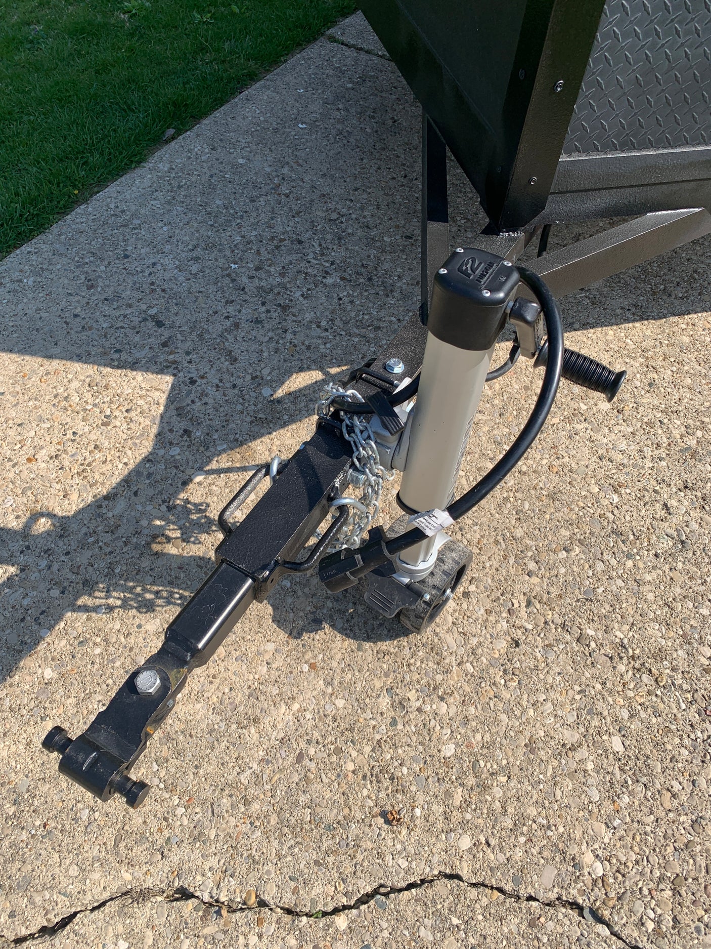 Up-close of an RV rental trailer's front hitch, jack, safety chains & electrical connection on concrete.