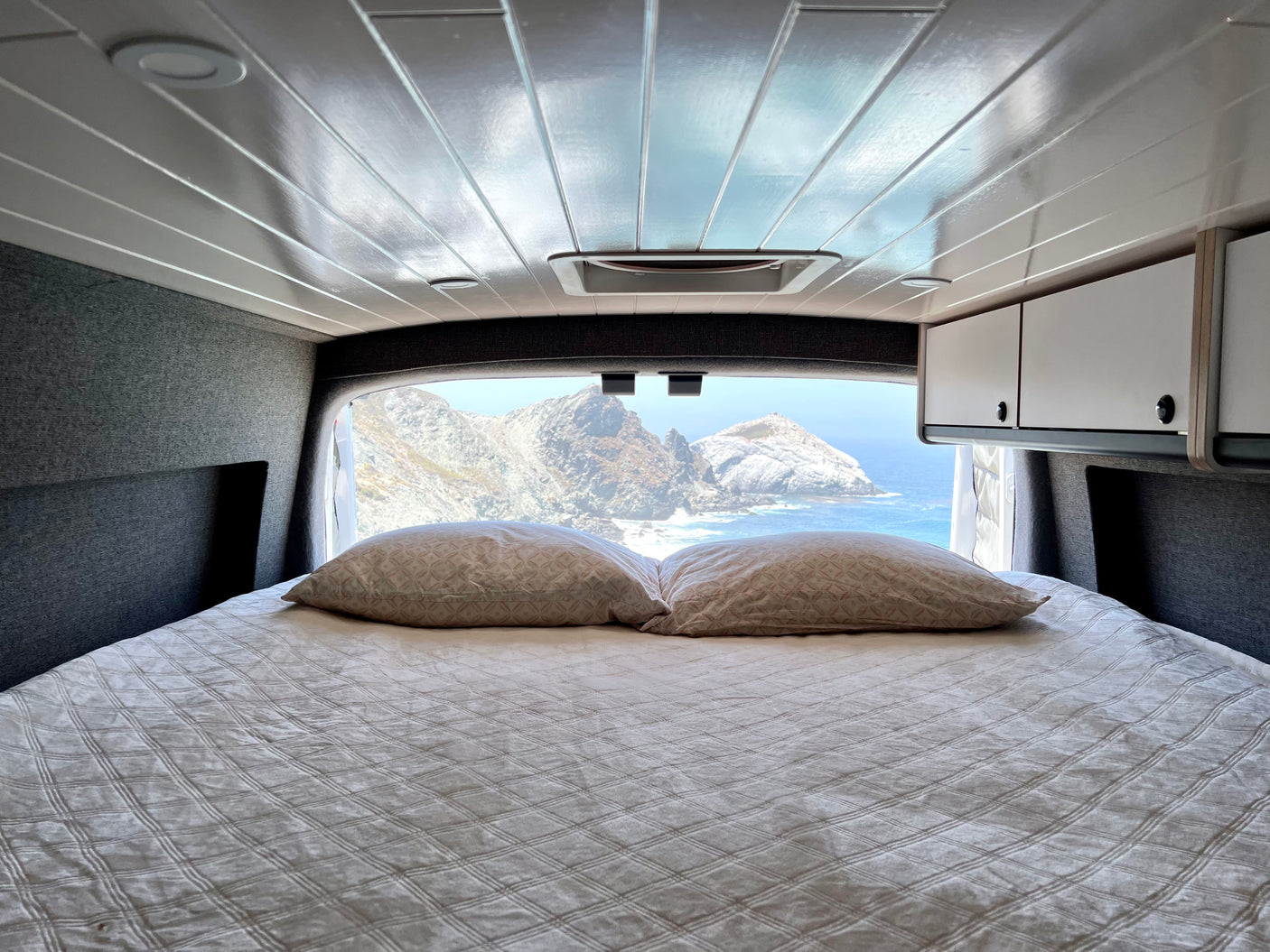 RV rental comfort: Enjoy breathtaking ocean views and rocky coastal mountains from your cozy bed in this camper van.