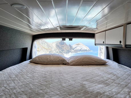 RV rental comfort: Enjoy breathtaking ocean views and rocky coastal mountains from your cozy bed in this camper van.