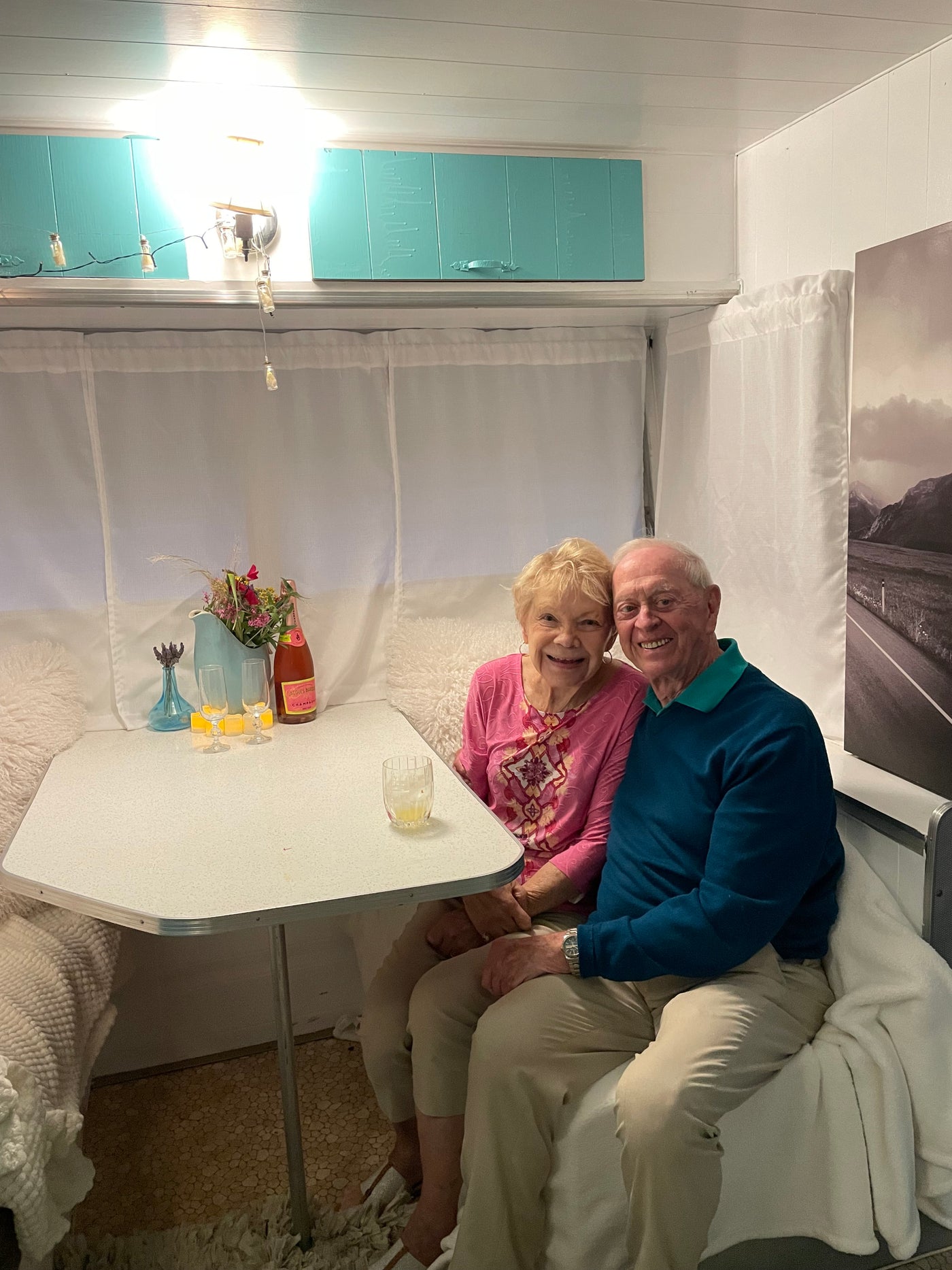 Beloved senior couple enjoying a delightful moment in their RV rental's cozy dinette, with drinks & flowers. — photo 6