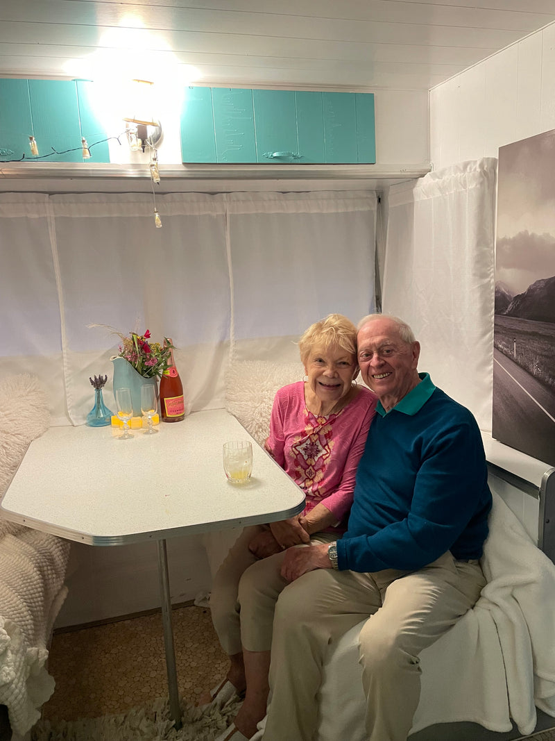 Beloved senior couple enjoying a delightful moment in their RV rental's cozy dinette, with drinks & flowers. — photo 6