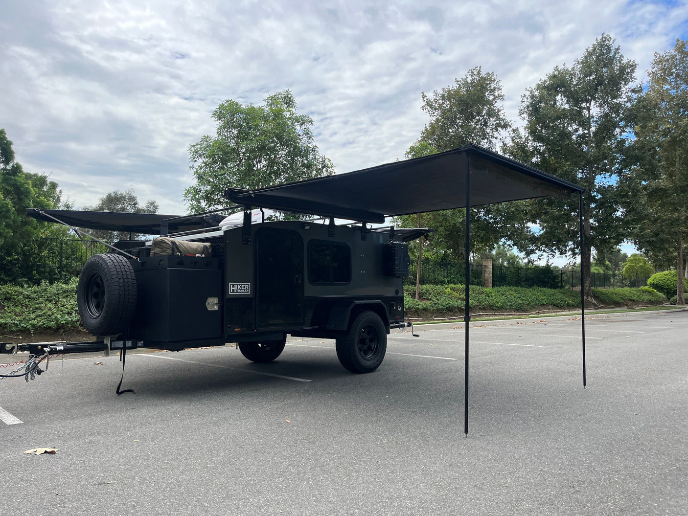 Dark Hiker Trailer RV rental, an off-road camper with extended awnings for shade, parked in a lot, ready for adventure.