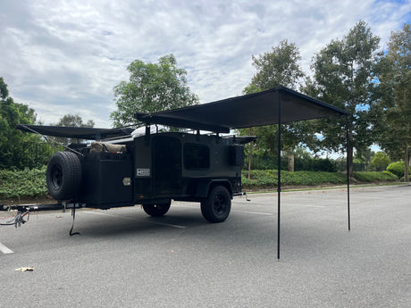 Dark Hiker Trailer RV rental, an off-road camper with extended awnings for shade, parked in a lot, ready for adventure.