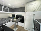 Cozy compact RV rental interior featuring a pop-top roof, comfortable bed, and functional dining area.