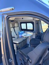 Inside a comfortable rv rental camper van: view of passenger seats, table, window, and controls for your road trip.