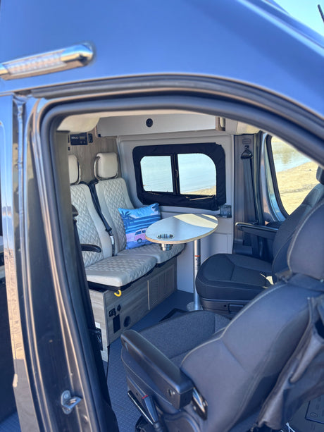 Inside a comfortable rv rental camper van: view of passenger seats, table, window, and controls for your road trip.
