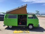 Bright green VW Westfalia pop-top camper van, an ideal RV rental for a beach getaway. Parked by the ocean with a lifeguard tower.