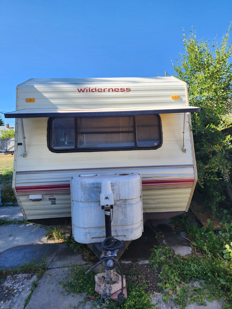  sits in a grassy field with trees.|This white Wilderness travel trailer — photo 1