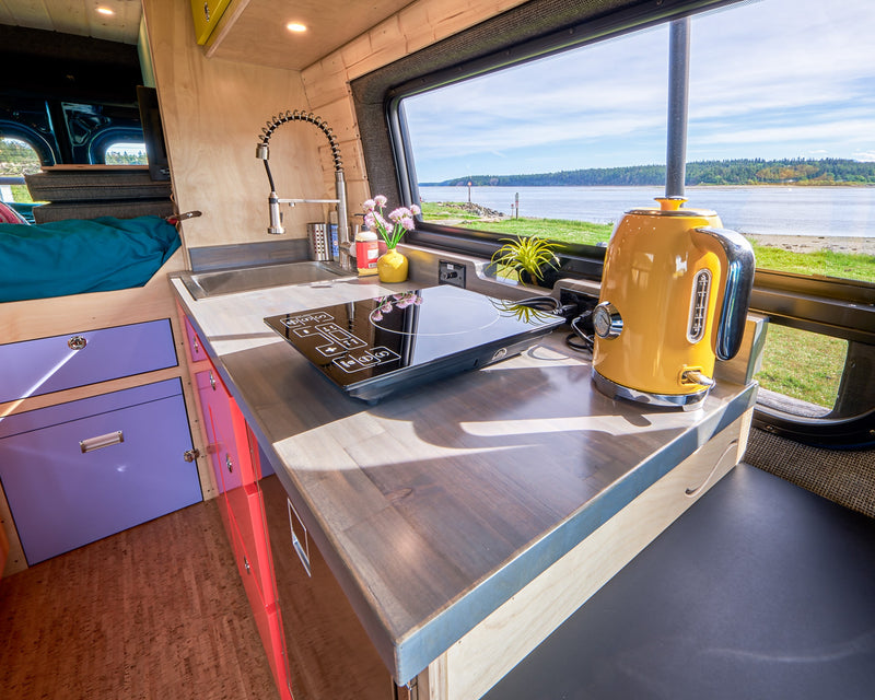 RV rental kitchen with sink, induction cooktop, and a yellow kettle, offering a scenic waterfront view. — photo 19