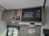 RV rental interior: kitchen with built-in microwave, light wood cabinets, and range hood. Compact camper design.