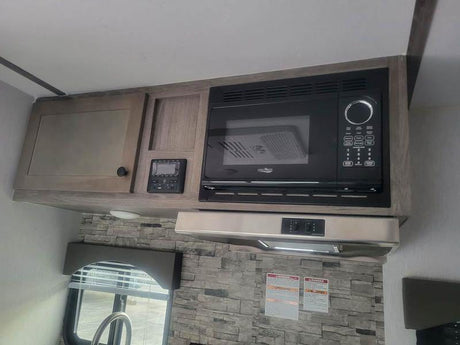 RV rental interior: kitchen with built-in microwave, light wood cabinets, and range hood. Compact camper design.