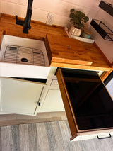 Modern RV rental kitchen featuring a pull-out induction cooktop, farmhouse sink, and light wood counters.
