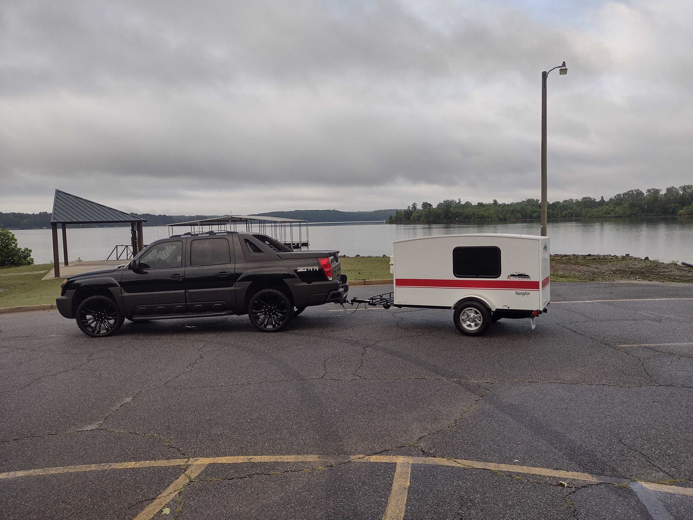 Black truck towing a Runaway RV rental trailer by a lake. Perfect for outdoor camping adventures!