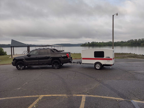 Black truck towing a Runaway RV rental trailer by a lake. Perfect for outdoor camping adventures!