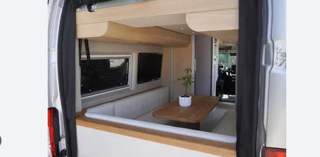RV rental: Modern camper van interior, featuring a dining area with a wooden table, padded benches, window, and TV.