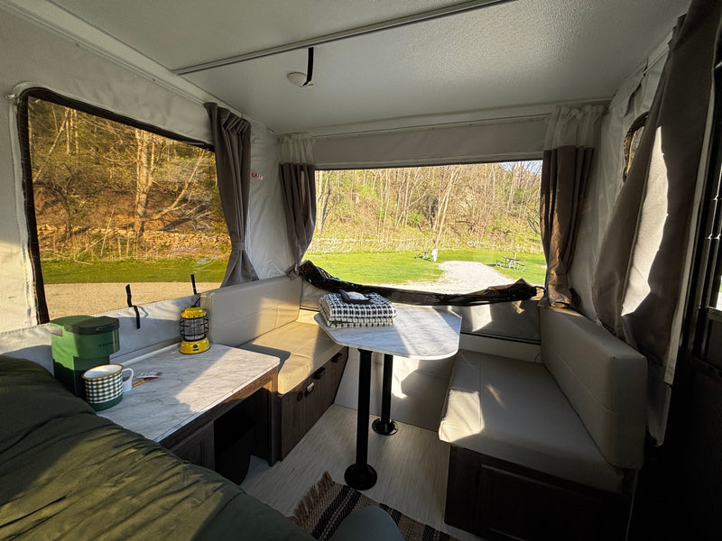 Cozy RV rental interior with a dinette, Keurig, and lantern, offering a serene view of a campsite and nature outside. — photo 4