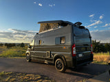 Grey Winnebago Solis camper van with pop-top extended, parked on asphalt in scenic outdoor setting. Perfect for an RV rental adventure.