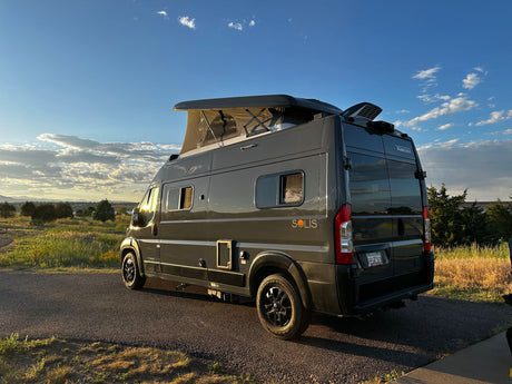 Grey Winnebago Solis camper van with pop-top extended, parked on asphalt in scenic outdoor setting. Perfect for an RV rental adventure.