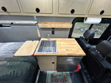 This RV rental offers a well-equipped camper van kitchenette with sink, wood counter, and comfortable bed.