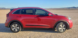 Red car, not an RV rental, on cracked desert ground with mountains under a clear sky. Ready for travel adventure.