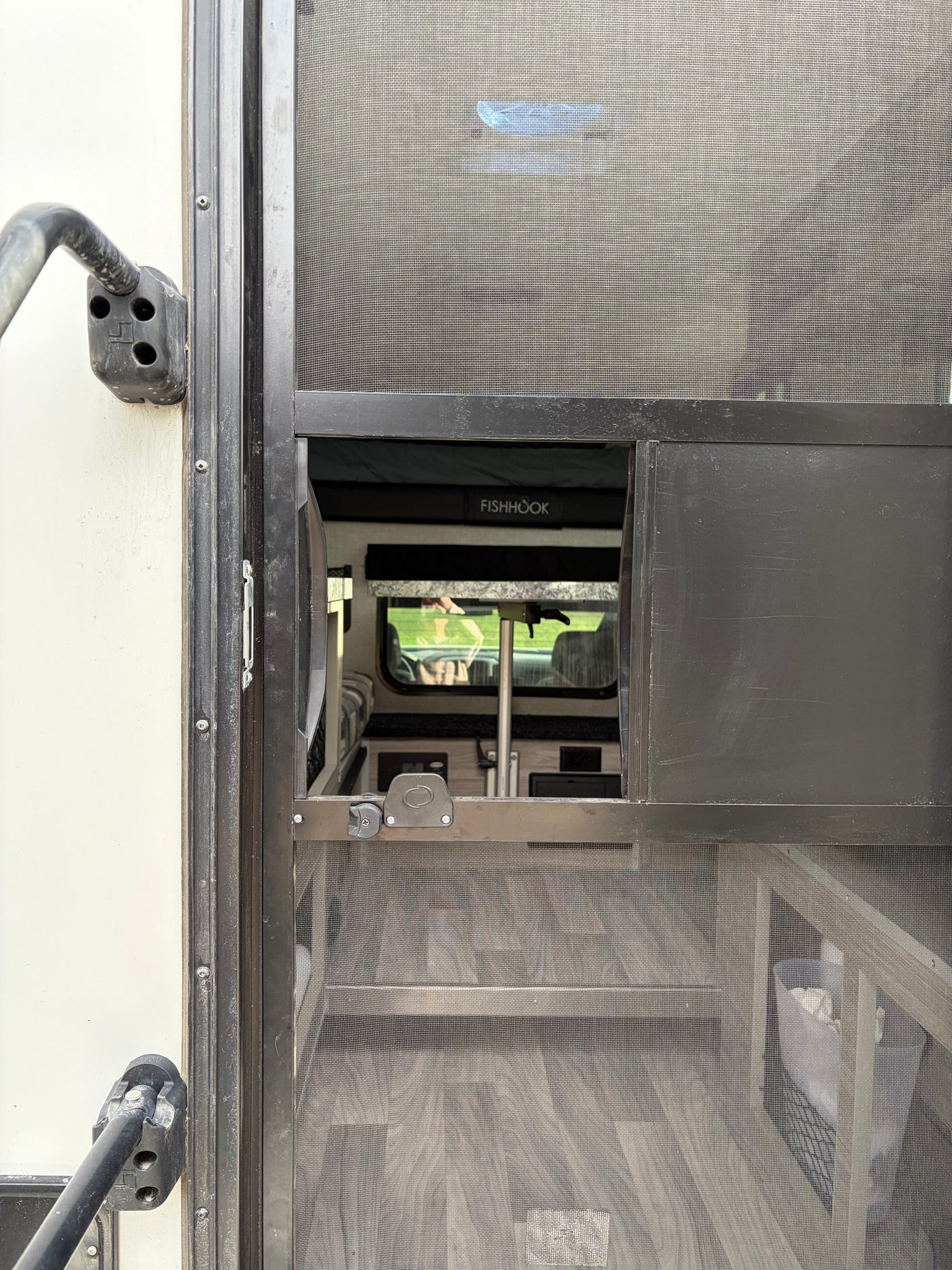 Inside an RV rental through a screen door: view of the interior with a "FISHHOOK" bunk, table, and flooring.