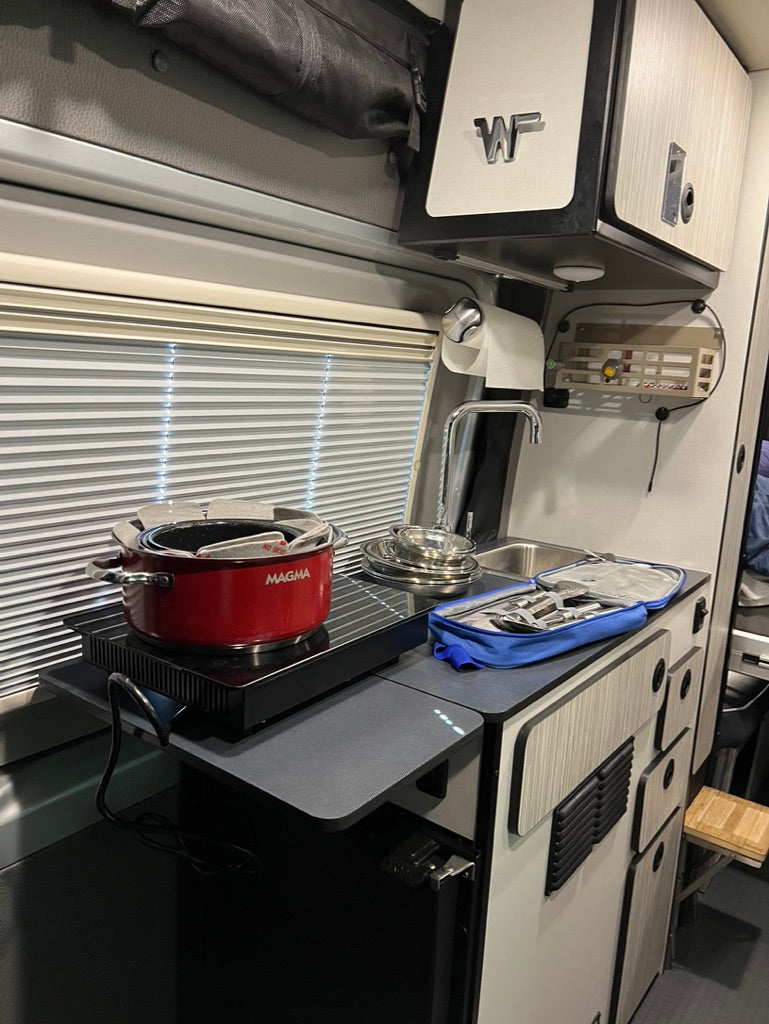 RV rental interior shows a compact kitchen galley with an induction cooktop, red pot, sink, and storage cabinets.