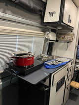 RV rental interior shows a compact kitchen galley with an induction cooktop, red pot, sink, and storage cabinets.
