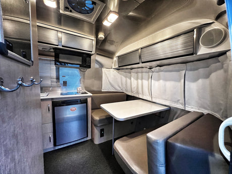 RV rental interior: A compact camper living area featuring a kitchenette with fridge and microwave, plus a dinette with bench seating.