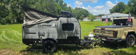 A gray Coachmen Clipper pop-up travel trailer hitched to a tan Jeep Gladiator. Ideal RV rental for off-road camping adventures.