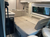RV rental interior featuring a versatile bed/seating area, compact kitchenette, and window with outdoor views.