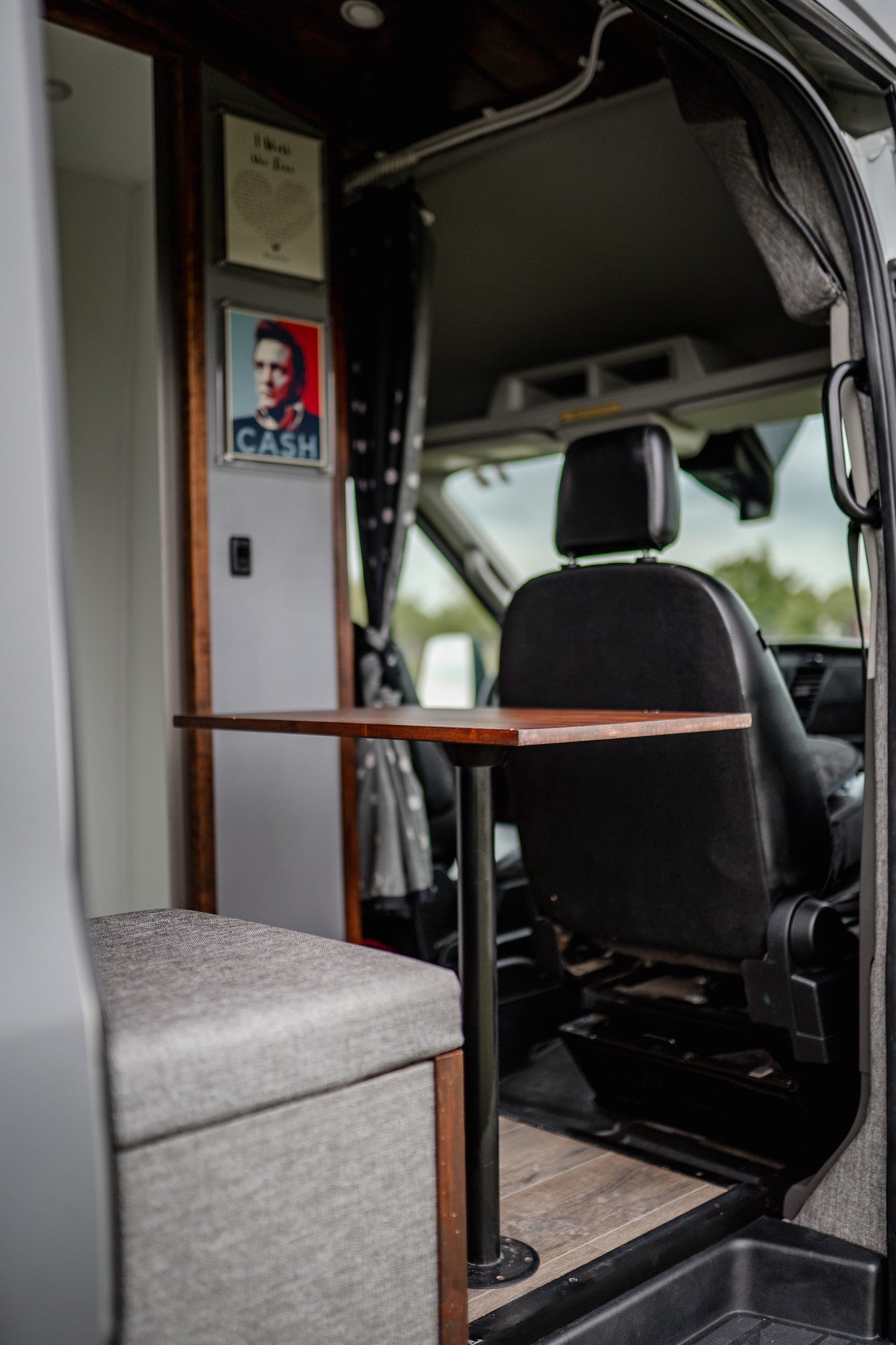 This RV rental features a cozy dining area with a table, padded bench, and unique wall decor, including Johnny Cash.